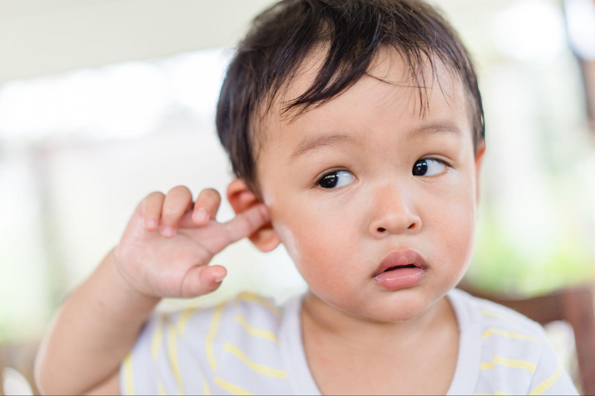 A little boy putting his finger in his ear